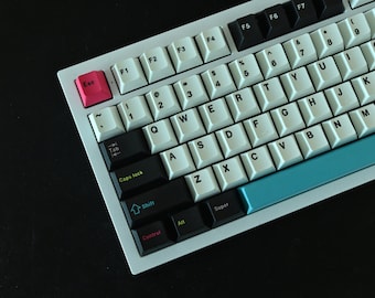 May include: A white mechanical keyboard with black keys and a blue space bar. The keys have black lettering and the function keys are labelled F1 to F7. The keyboard has a white frame and a black base.