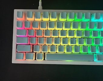 Może przedstawiać: Biała mechaniczna klawiatura z podświetleniem klawiszy w kolorach tęczy. Klawisze są oznaczone standardowym układem QWERTY.