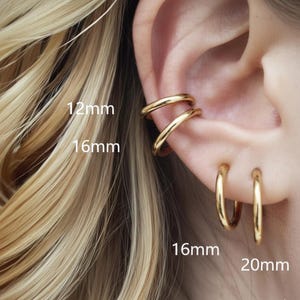 Könnte beinhalten: Goldfarbener Ohrschmuck, darunter zwei Ohrklemmen und zwei Creolen. Die Ohrklemmen sind 12 mm und 16 mm groß. Die Creolen sind 16 mm und 20 mm groß. Der Schmuck wird an einem Ohr gezeigt.