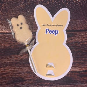 May include: A yellow bunny-shaped card with the word "Peep" in blue and the text "A Sweet Treat for my favorite". A marshmallow peep on a stick is in a clear wrapper.