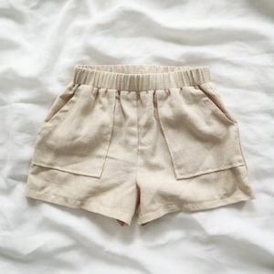 May include: Beige linen shorts with two large pockets and an elastic waistband.