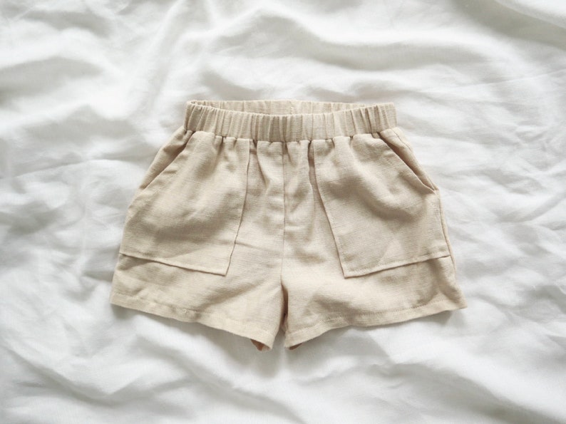 May include: Beige linen shorts with two large pockets and an elastic waistband.