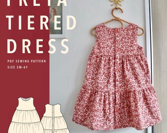 May include: A sleeveless tiered dress with a red and white floral pattern hanging on a wooden hanger. The text reads FREYA TIERED DRESS, PDF SEWING PATTERN, SIZE 3M-6Y. Below the text are two line drawings showing the front and back of the dress design.