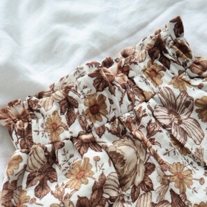 May include: A white fabric with a brown floral pattern. The fabric has a ruffled edge and is gathered at the waist.