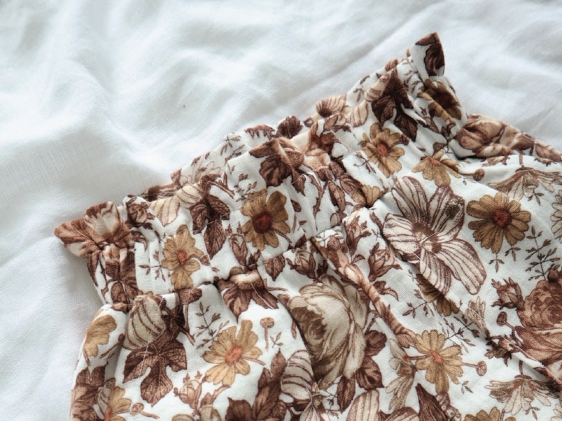 May include: A white fabric with a brown floral pattern. The fabric has a ruffled edge and is gathered at the waist.