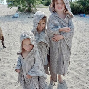 Puede incluir: Tres ponchos con capucha confeccionados en tela de color beige claro con textura de gofre. Cada poncho presenta un corte holgado y drapeado con mangas anchas y una capucha profunda. El material texturizado tiene un patr&oacute;n de cuadr&iacute;cula.