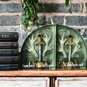 May include: Green bookends with gold accents and a sword design. The bookends are shaped like antlers and have the text "i am here i am with you... to whatever end" on the front.