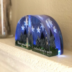 May include: Two clear resin bookends shaped like half circles with a blue and white starry night sky design. The bookends have a quote from the movie "The Princess Bride" that reads "I've been looking for you, you know."