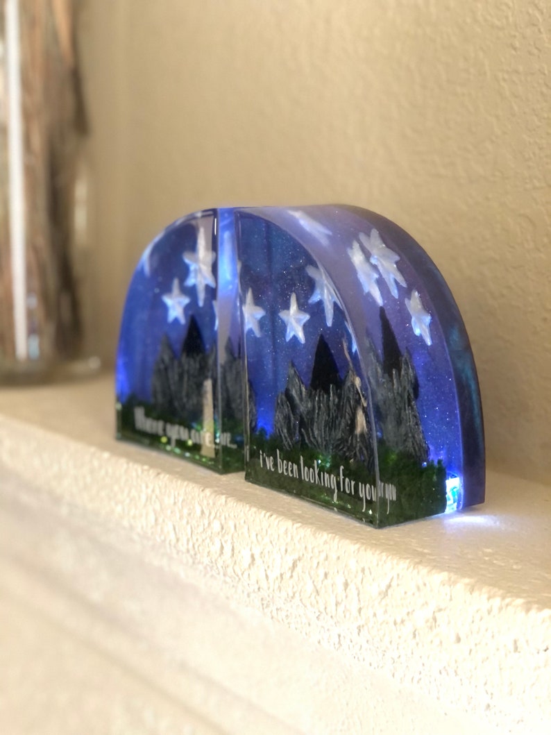 May include: Two clear resin bookends shaped like half circles with a blue and white starry night sky design. The bookends have a quote from the movie "The Princess Bride" that reads "I've been looking for you, you know."