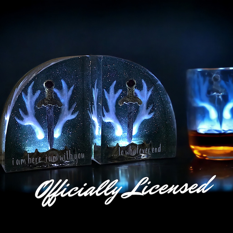 May include: A pair of bookends with a glowing blue design of antlers and a sword. The bookends are made of clear resin and have the text "I am here I am with you... to whatever end" on them.