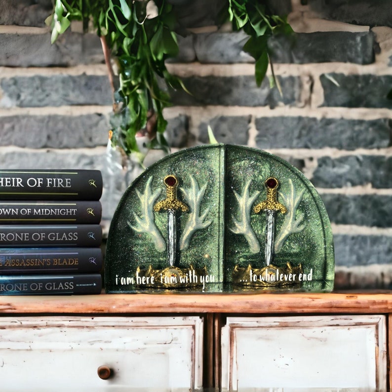 May include: Green bookends with gold accents and a sword design. The bookends are shaped like antlers and have the text "i am here i am with you... to whatever end" on the front.