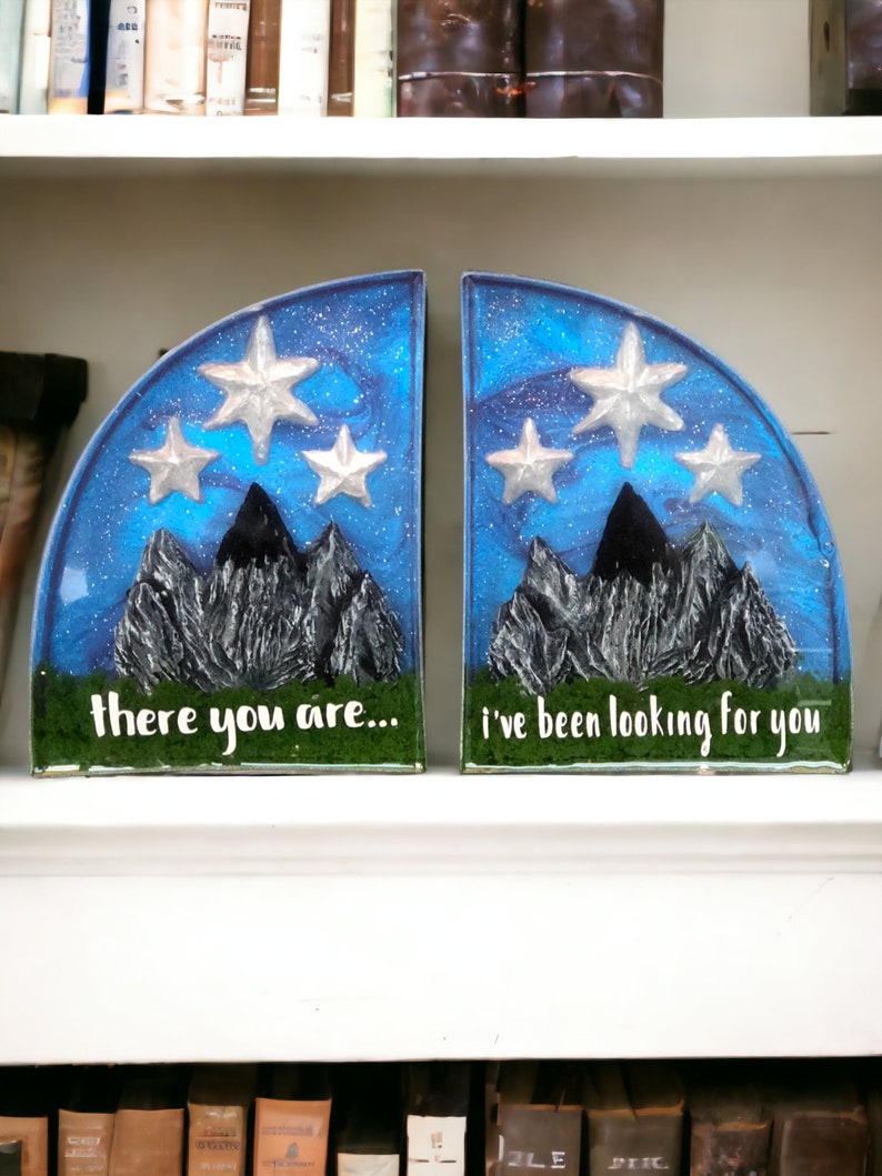 May include: A pair of blue and silver bookends shaped like a mountain range with stars in the sky. The left bookend says "there you are..." and the right bookend says "i've been looking for you".