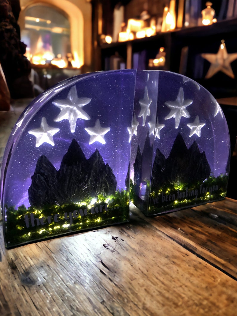 May include: Two bookends made of clear resin with a purple and black mountain scene and white stars. The bookends are lit from within and the text "there you are..." and "I've been looking for you" are visible on the front of each bookend.