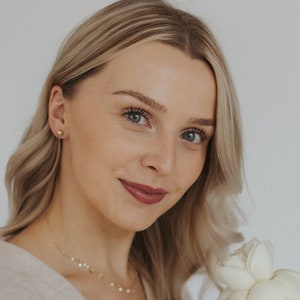 May include: A woman with blonde hair is smiling and holding a bouquet of white roses.