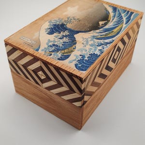 May include: A wooden box with a geometric pattern on the sides and a printed image of the Great Wave off Kanagawa on the top.
