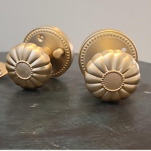 May include: Two gold door knobs with a decorative, scalloped design. The knobs have a beaded trim around the edge.