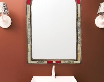 May include: An arched mirror with a decorative frame featuring red and cream accents. The mirror is mounted above a white sink with a geometric patterned countertop. Two sconces with patterned shades flank the mirror.