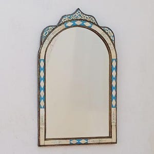 May include: An arched mirror with a decorative frame. The frame features a white and blue diamond pattern with ornate detailing at the top. The mirror is rectangular with rounded top edges.