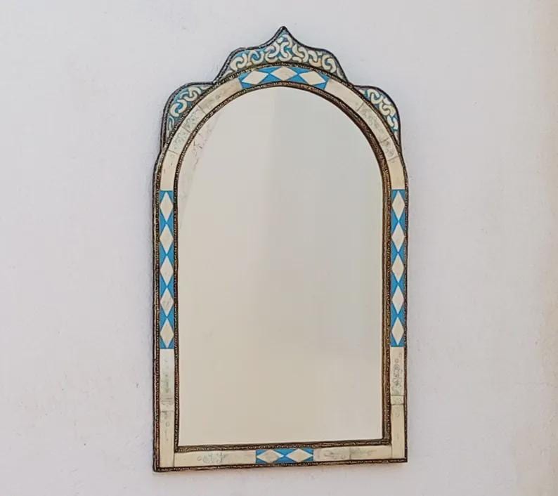 May include: An arched mirror with a decorative frame. The frame features a white and blue diamond pattern with ornate detailing at the top. The mirror is rectangular with rounded top edges.