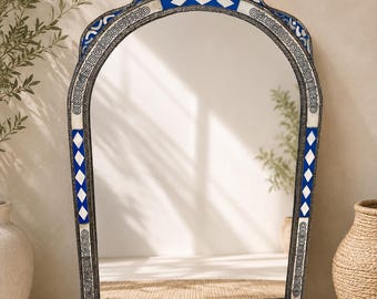 May include: An arched wall mirror featuring a decorative frame with inlaid blue and white geometric patterns. The frame displays intricate silver-toned metalwork with repeating circular motifs and diamond-shaped accents along the border.