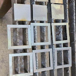 K&ouml;nnte beinhalten: Nahaufnahme von neun Metallquadraten, einige mit Rahmen und einige massiv, in Reihen auf einer Metalloberfl&auml;che angeordnet. Die Quadrate sind in verschiedenen Graut&ouml;nen und Braunt&ouml;nen gehalten.