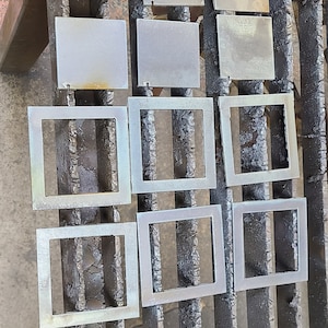 K&ouml;nnte beinhalten: Neun Metallquadrate mit leicht strukturierter Oberfl&auml;che sind in drei Reihen zu je drei auf einem schwarzen Metallgitter angeordnet. Die Quadrate sind alle gleich gro&szlig; und gleich geformt und gleichm&auml;&szlig;ig verteilt.