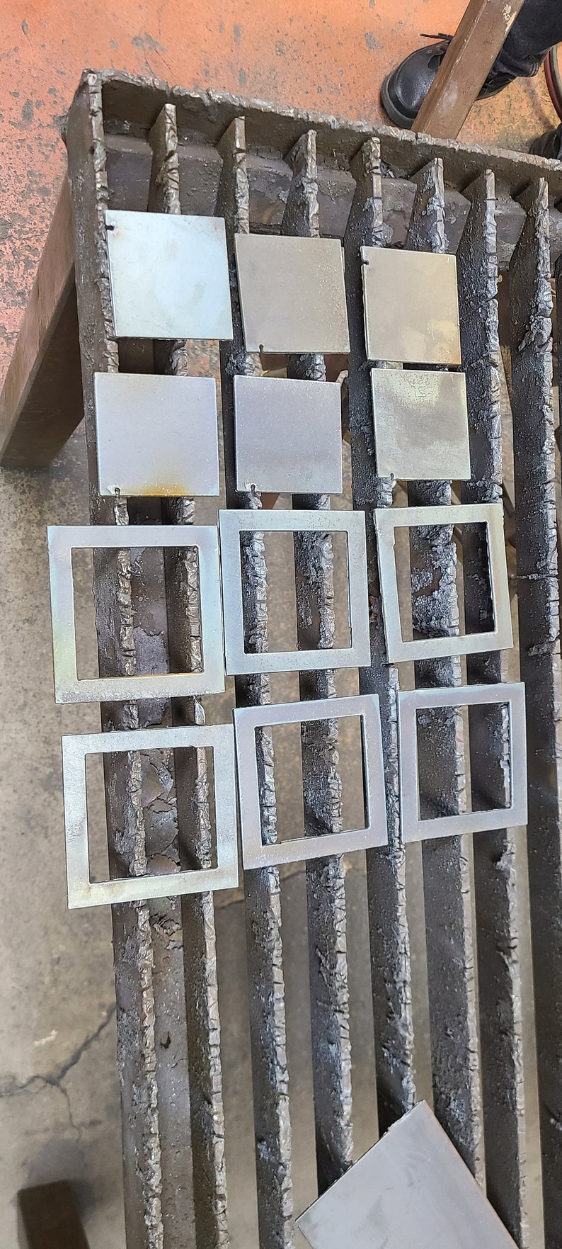 K&ouml;nnte beinhalten: Neun Metallquadrate mit leicht strukturierter Oberfl&auml;che sind in drei Reihen zu je drei auf einem schwarzen Metallgitter angeordnet. Die Quadrate sind alle gleich gro&szlig; und gleich geformt und gleichm&auml;&szlig;ig verteilt.