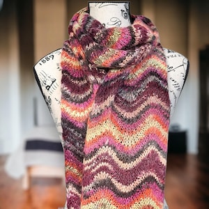 May include: A colorful knitted scarf with a chevron pattern in shades of pink, orange, brown, and gray.