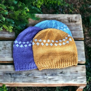 May include: Three knitted hats in different colors: purple, yellow, and blue. Each hat has a white pattern of small flowers around the brim.