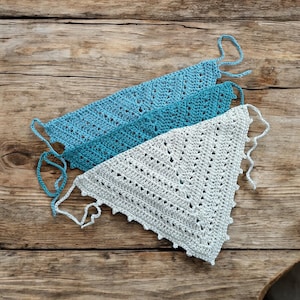 May include: Three crocheted triangular scarves in shades of blue and white. The scarves are layered on top of each other and have a delicate, lacy pattern.