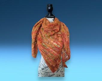 Puede incluir: Un chal triangular en tonos naranja, rojo y amarillo con un patrón de punto de encaje. El chal está drapeado sobre un maniquí blanco con un soporte negro.