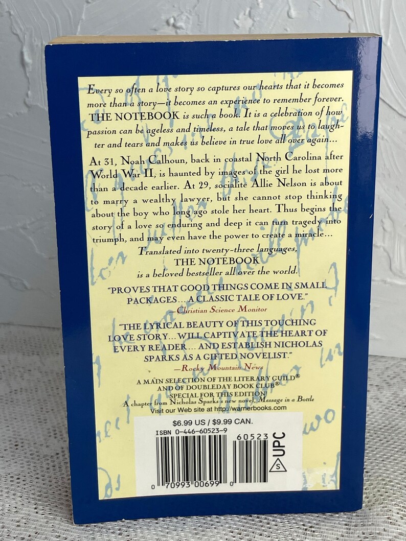 May include: A paperback copy of "The Notebook" by Nicholas Sparks. The book's back cover features text describing the story of Noah and Allie, set against a blue background. Includes quotes and a barcode.