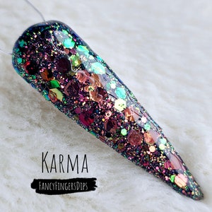 May include: A long, pointed, black nail with a multi-colored glitter polish. The nail is decorated with a variety of small, iridescent glitter pieces. The text "KARMA" and "FANCYFINGERSDIPS" is written below the nail.