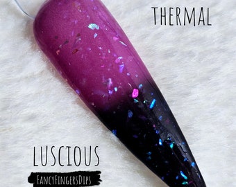 Puede incluir: Un polvo de inmersión para uñas térmico en un degradado de color de morado oscuro a negro con purpurina iridiscente. La inmersión para uñas se llama "Luscious" y es de la marca "FancyFingersDips".