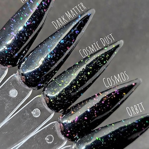 May include: Five black nail polish bottles with different coloured glitter. The bottles are labelled "Milky Way", "Dark Matter", "Cosmic Dust", "Cosmos", and "Orbit".