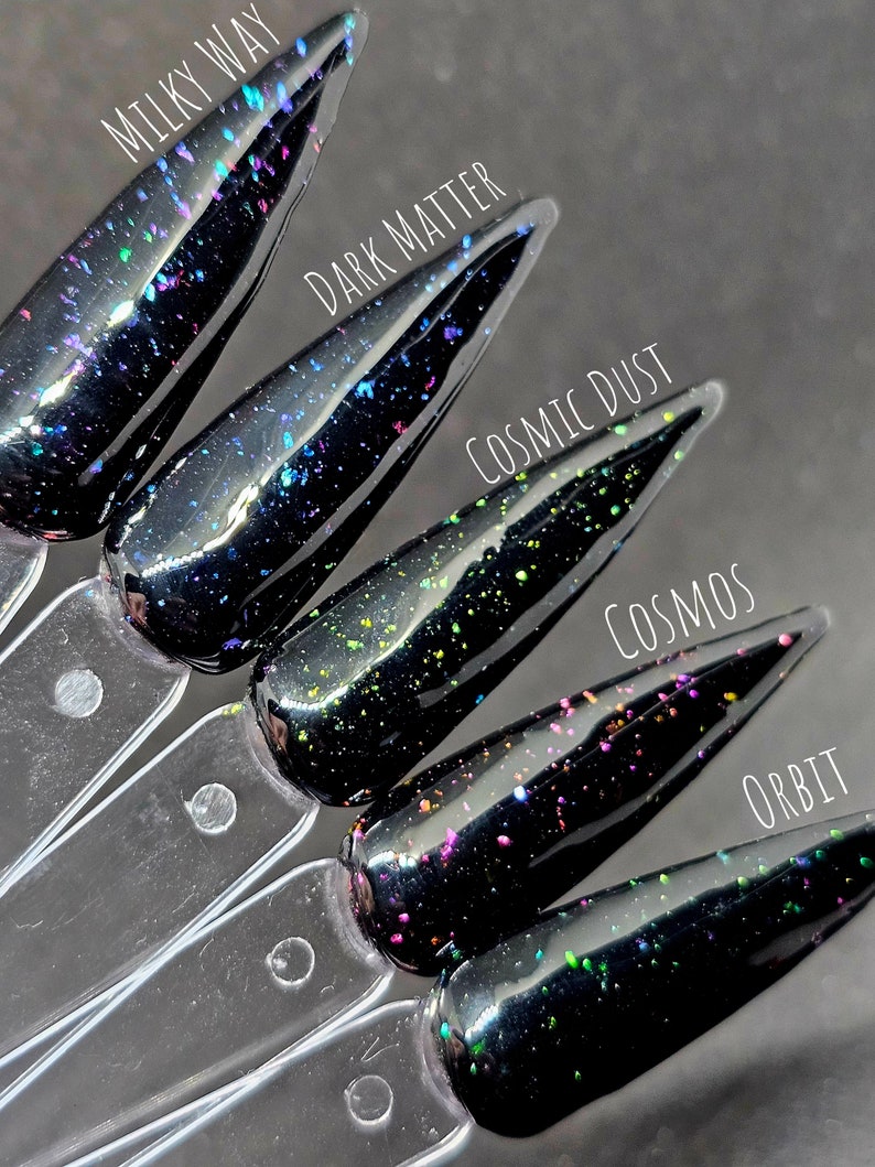 May include: Five black nail polish bottles with different coloured glitter. The bottles are labelled "Milky Way", "Dark Matter", "Cosmic Dust", "Cosmos", and "Orbit".