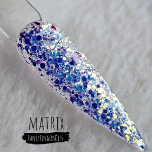 Puede incluir: Un baño de inmersión para uñas transparente con purpurina azul, morada y dorada iridiscente. El baño se llama "Matrix" y es de la marca "FancyFingersDips".