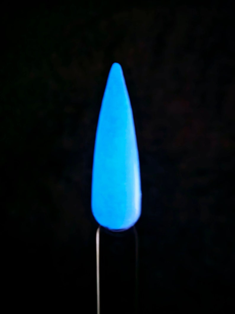 May include: A single, glowing blue nail tip against a black background. The nail is a vibrant, light blue color, and appears to be illuminated from within. The nail is mounted on a thin, black stick.