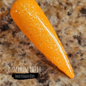 Puede incluir: Primer plano de un polvo de inmersión para uñas de color naranja brillante con un acabado brillante. El texto "PUMPKIN PATCH" y "FANCYFINGERSDIPS" es visible en la imagen.