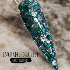 May include: A close-up of a green and silver glitter nail dip powder. The powder is called "Enchanted Forest" and is from the brand "FancyFingersDips".