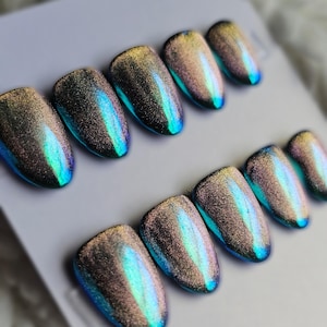 May include: A set of ten almond-shaped press-on nails featuring a magnetic cat-eye finish. The nails display a shifting color gradient that transitions from deep charcoal and bronze tones to vibrant metallic blue and green highlights.