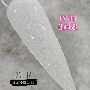 Könnte beinhalten: Ein weißer Nagellack mit schimmerndem Glitzer. Der Lack ist ein UV-Sonnenwechsler, das heißt, er ändert seine Farbe in der Sonne. Der Lack ist mit "Dahlia" und "FancyFingersDips" gekennzeichnet.