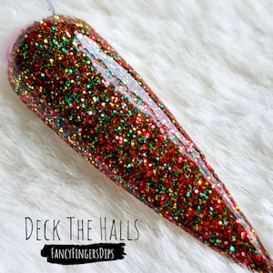 May include: A long, pointed, red, green, and gold glitter nail with a clear top coat. The text "DECK THE HALLS" and "FANCYFINGERSDIPS" is below the nail.