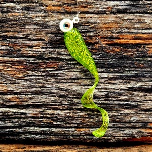 May include: A green and yellow soft plastic fishing lure with a white eye and a silver hook.