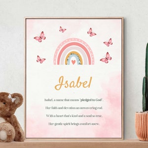 May include: A framed print featuring the name "Isabel" in gold script, with a rainbow and butterflies design. The print includes a poem about the name, set against a soft pink watercolor background. A wooden frame surrounds the artwork.