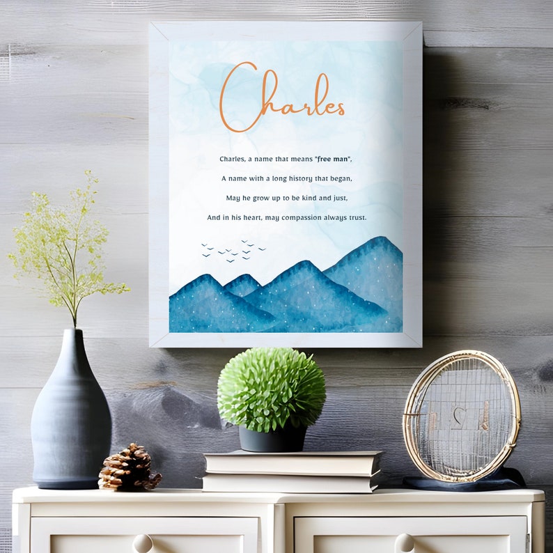 Puede incluir: Una impresi&oacute;n de acuarela con un paisaje de monta&ntilde;a azul y el nombre "Charles" en texto naranja. El texto debajo dice "Charles, un nombre que significa 'hombre libre', Un nombre con una larga historia que comenz&oacute;, Que crezca para ser amable y justo, Y en su coraz&oacute;n, que la compasi&oacute;n siempre conf&iacute;e."