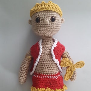 May include: A crocheted doll with a yellow crown, red and white vest, and red skirt with a yellow trim. The doll is holding a yellow crocheted butterfly.
