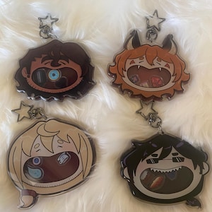 May include: Four cartoon character keychains with star-shaped clasps. Each keychain features a different character design with a unique hairstyle and facial expression. The characters are in various colors, including brown, orange, blonde, and black.