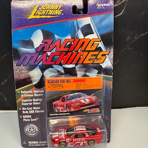 Peut inclure: Une voiture de course jouet en métal moulé sous pression rouge et blanche, présentée dans son emballage d'origine. L'emballage présente le logo "Johnny Lightning" et les mots "Racing Machines". La voiture porte le numéro 8.