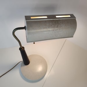 May include: A vintage desk lamp with a white metal shade and a black and gold base. The shade has a textured surface and two rectangular openings that allow light to shine through.